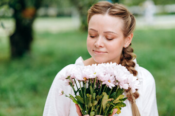 Beautiful girl with closed eyes sniffs beautiful white flowers outdoors