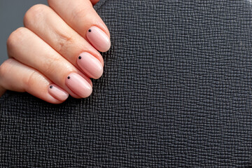 Female hand with black leather surface with trendy beautiful manicure - pink nude nails with black small dots with copy space. Selective focus. Closeup view