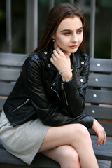 Fashion portrait of young elegant brunette woman outdoor. black leather jacket, clutch bag.