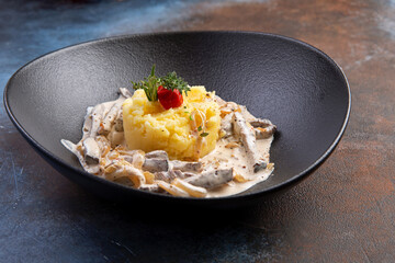 Beef stroganoff with mashed potatoes in a dark plate