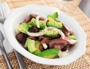 salad of black tomatoes, avocado and onions in white ceramic bowl
