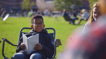 Curious kids sitting with workbooks on folding chairs while listening to teacher at outdoor lesson