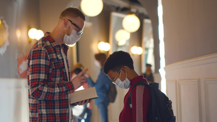 Side view of young teacher in mask scolding african schoolboy for bad behavior