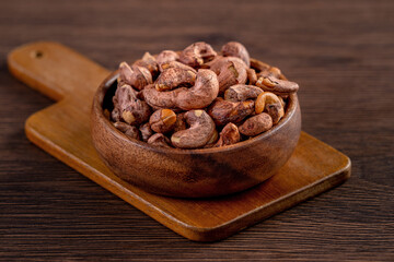 Cashew nuts with peel in a wooden bowl on wooden tray and table background, healthy raw food plate.