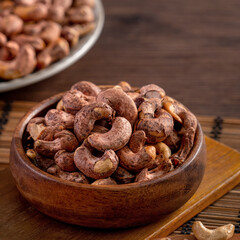 Cashew nuts with peel in a wooden bowl on wooden tray and table background, healthy raw food plate.