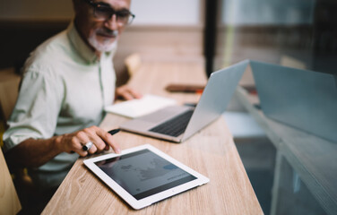 Crop businessman using tablet and laptop in creative workplace