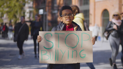 Portrait of african preteen boy standing outdoors school building with stop bullying cardboard sign