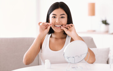 Young asian lady using dental floss looking in mirror