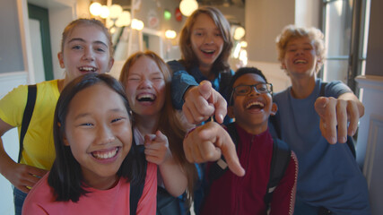 Group of diverse children laughing and pointing at you standing in school corridor