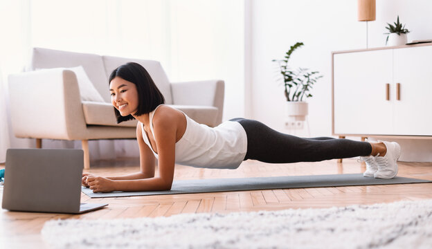 Sporty asian woman doing plank watching tutorial on laptop