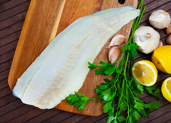 Fresh cod fillet on wooden surface with seasonings ready for cooking..