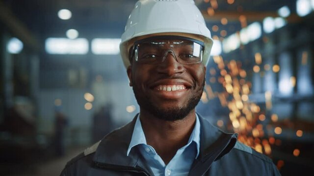 Happy Professional Heavy Industry Engineer/Worker Wearing Uniform, Glasses and Hard Hat in a Steel Factory. Smiling African American Industrial Specialist Standing in a Metal Construction Manufacture.