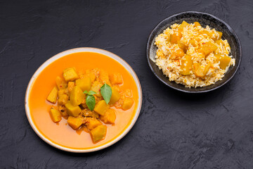 Curry or pumpkin soup with rice served in a ceramic platter on a black background - top view with writing space.