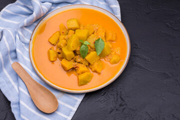 Curry or pumpkin soup served in a ceramic plate with a spoon placed on a black background - top view with space for writing messages.