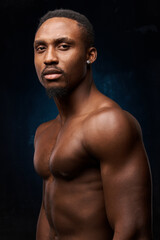 Fototapeta na wymiar dark-skinned handsome man with a naked sports torso.on a dark background, he looks at the camera