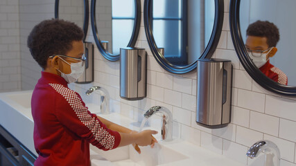 African student in safety mask washing hands in modern school restroom
