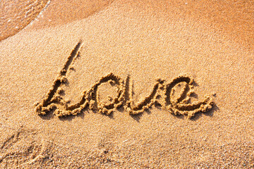 Word Love handwritten on a sandy beach