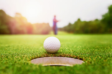 close up golf ball on green grass with sunrise background