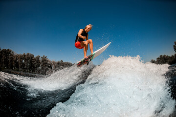 view of athletic man on surf style wakeboard jumping over splashing wave