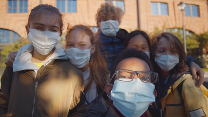 Multiethnic school children wearing protective face masks taking selfie outdoors