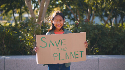 Portrait of cute teenage asian girl holding save the planet sign protesting for nature outdoors