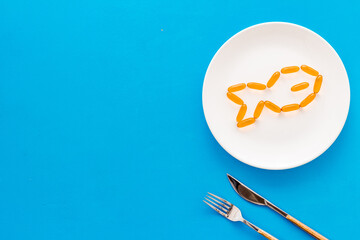 Omega cod liver oil capsules on plate with fish shape, top view