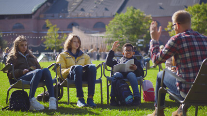 Back view of male teacher conducting lesson with children in city park