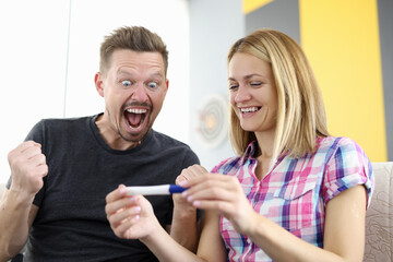 Smiling husband and wife are looking at pregnancy test. Family planning concept.