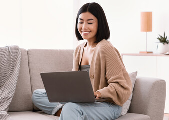 Naklejka premium Asian woman sitting on couch and working on pc
