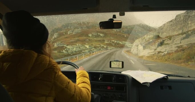 Woman drive camping van on epic mountain road. Living van life on wheels, during road trip across USA or Iceland. Female traveller drive RV van to camping site, use smartphone gps and map