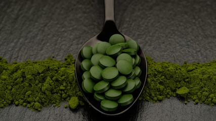 chlorella or spirulina superfoods tablets in wooden spoon and powder on background