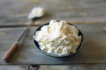 Fresh mascarpone cheese in a bowl on a wooden surface. Selective focus. Macro.