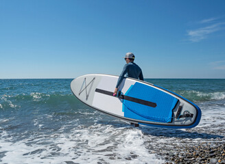 Man with SUP on beach go surfing at summer sunny day