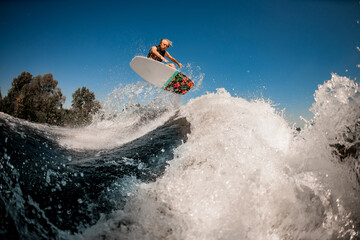 Fototapeta na wymiar Beautiful view of man on surf style wakeboard masterfully jumping over splashing wave