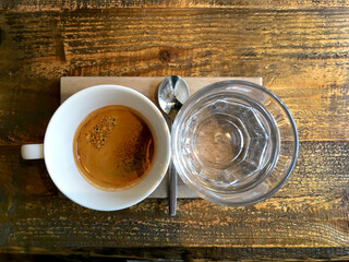 White coffee cup and glass of water and spoon on wooden table. Top view.