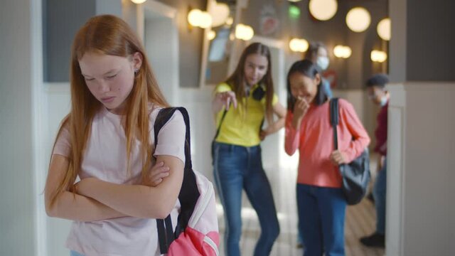 Unhappy schoolgirl being gossiped and laughed at by classmates