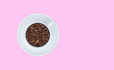 White Cup and saucer, full Cup of coffee beans. Top view, pink background. Free space for text.