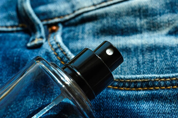 Glass bottle of unisex fragrant perfume or scented toilet water on a blue denim. Casual light scent...