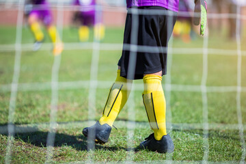 Selective focus to soccer goalkeeper with blurry mesh of goal. Soccer ball training in academy.