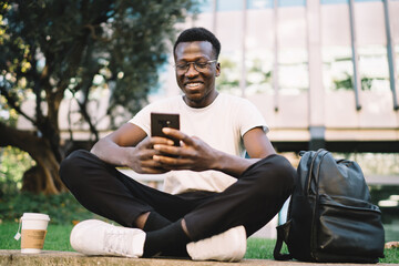 Happy ethnic man messaging on cellphone on street