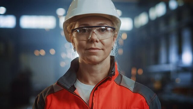 Portrait of a Professional Heavy Industry Engineer/Worker Wearing Uniform, Glasses and Hard Hat in a Steel Factory. Beautiful Female Industrial Specialist Standing in Metal Construction Facility.