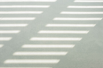Hard, diagonal floor shadows on gray tiles from window shutters or blinds. Attractive abstract half...