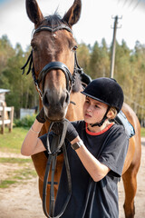 A girl in a black helmet leads a Bay horse on a warm early autumn day.