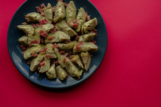 alcachofas con jam&oacute;n serrano saludable en plato azul con fondo rojo