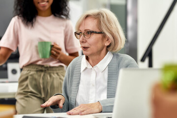 Close up of aged woman, senior intern talking to her young colleagues, Friendly workers listening to new employee during coffee break at work