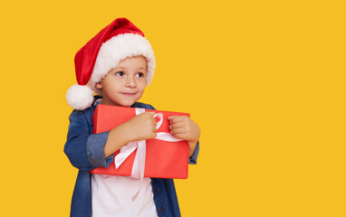 Portrait of a satisfied little child boy in christmas Santa hat. laughing isolated over yellow background. Holds a gift box. Preparing for the New Year holidays