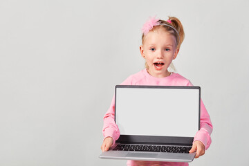 Closeup portrait of сute girl 4-5 year old in pink showing laptop screen with mock up on gray background