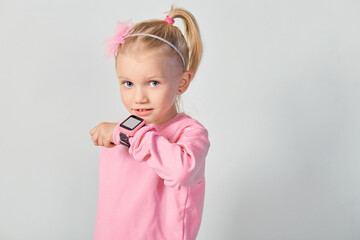 Cute caucasian little girl 4-5 year old wearing a smart watch on her wrist. Technology for children, against gray studio background