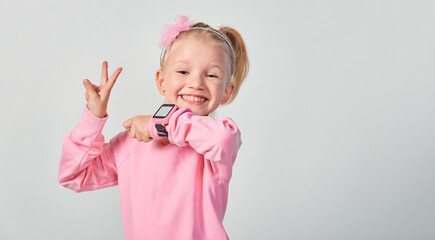 Cute caucasian little girl 4-5 year old wearing a smart watch on her wrist. Technology for children, against gray studio background