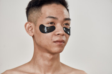 Portrait of shirtless young asian man with black patches under the eyes, looking away isolated over white background. Beauty, skincare routine, cosmetology for men